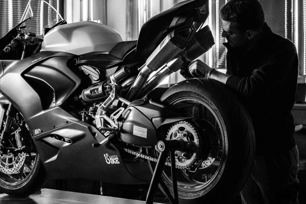 Ein Motorrad an dem ein Arbeiter eine Zard-Auspuffanlage montiert.